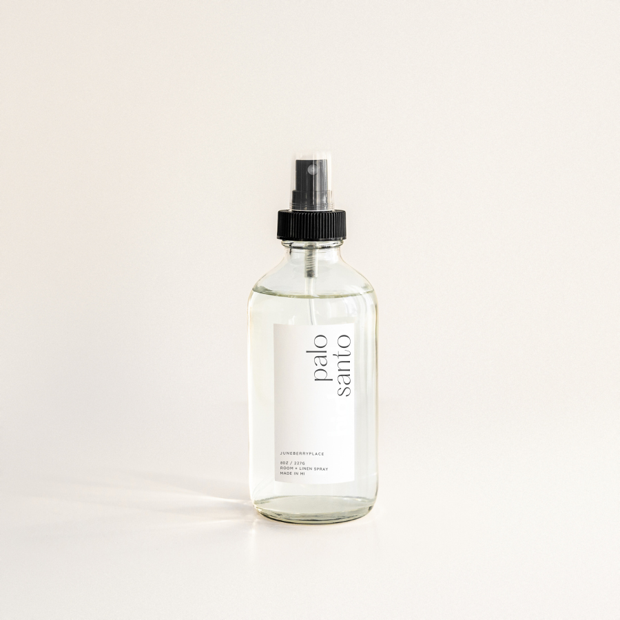 A clear spray bottle labeled 'PALO SANTO' with a black spray nozzle, placed against a neutral background.