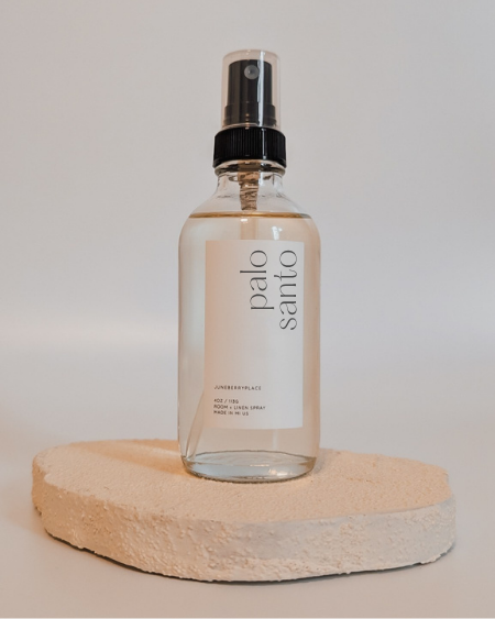 Clear spray bottle labeled 'palo santo' on a beige stone surface with a neutral background